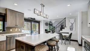Una cocina moderna con una isla grande, taburetes de bar, una zona de comedor y una escalera que sube a una buhardilla.