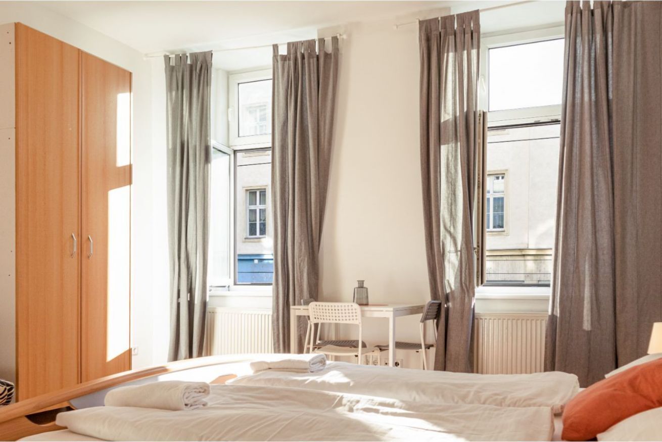 Un dormitorio con cama, escritorio, silla, armario de madera y ventana con cortinas.