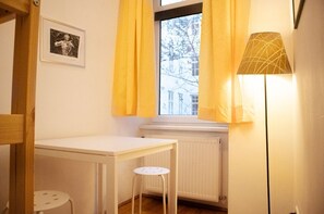 A room with a white radiator, a table, a small stool, and a floor lamp.