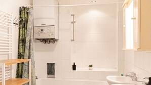 Ein Badezimmer mit einer Badewanne, zwei Waschbecken, einer Dusche, einer Toilette und einem Regal mit einer Pflanze.