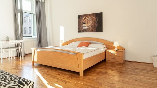 Ein Schlafzimmer mit einem hölzernen Bett, einem Schreibtisch, einem Sessel, einem Sofas mit ZEBRA-Muster und einem Löwenbild an der Wand.