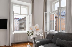 A modern living room with a sofa, a potted orchid, and a view of buildings through large windows.