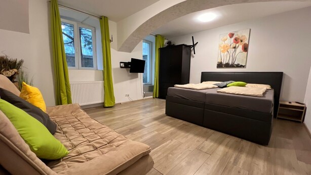 A modern bedroom with a sofa, a bed, a TV, and a painting.