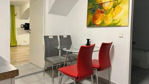 A dining area with a glass table, red and grey chairs, and a painting of tulips on the wall.