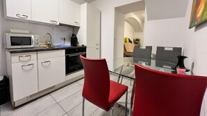 A compact kitchen with white cabinets, a microwave, and a coffee maker. There is a glass dining table with red chairs.