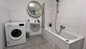 A modern bathroom with a washing machine, sink, and bathtub.
