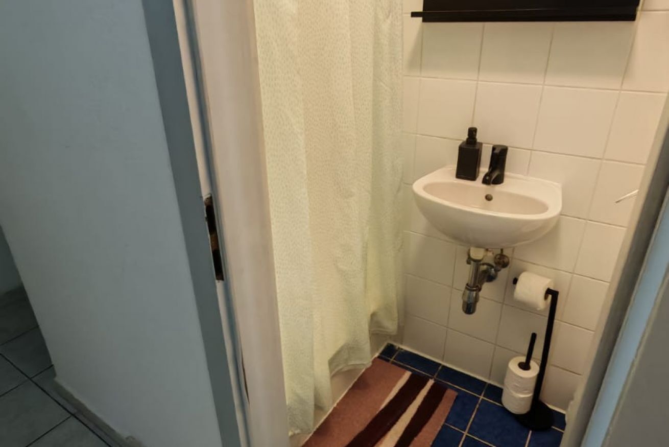 A bathroom with a white sink, a toilet, a towel rack, and a striped floor mat.
