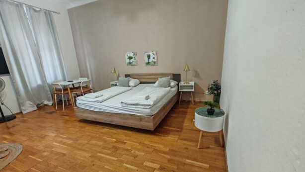 A bedroom with a wooden floor, a bed, a desk, two chairs, a small table, two bedside tables, and a potted plant. - Smart 2BR Apt. Perfect for Longstays near Rennweg (Vienna)