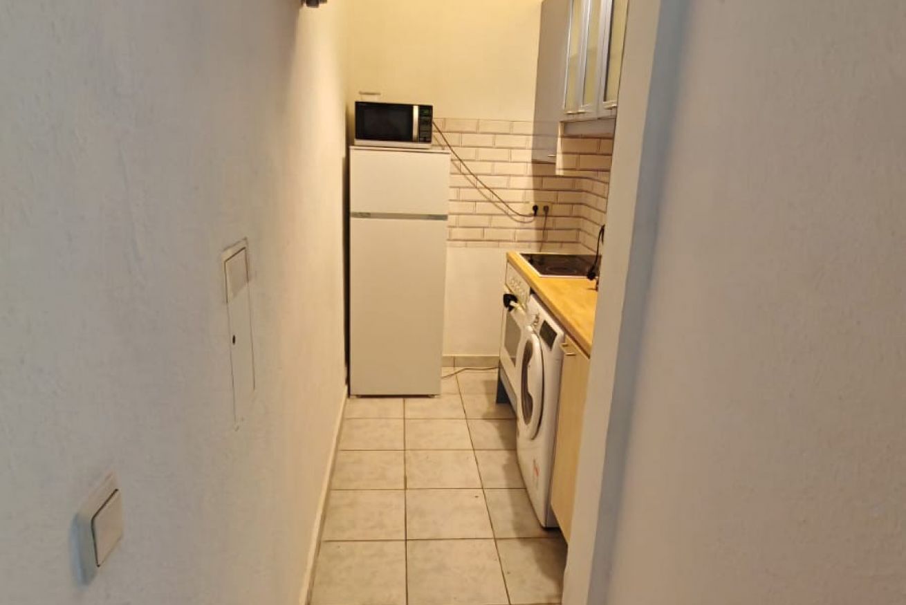 A compact kitchen with a refrigerator, microwave, washing machine, and a tiled backsplash.