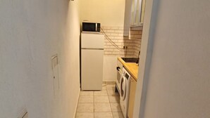 A compact kitchen with a refrigerator, microwave, washing machine, and a tiled backsplash. - Smart 2BR Apt. Perfect for Longstays near Rennweg (Vienna)