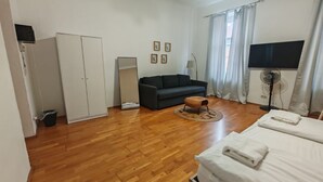 A room with a bed, a sofa, a wardrobe, a standing fan, and a TV. - Smart 2BR Apt. Perfect for Longstays near Rennweg (Vienna)