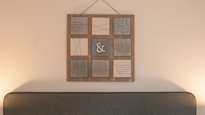 A wall-mounted wooden board with various text and symbols, including '&' and a heart symbol, on a plain wall.