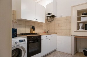 A compact kitchen with a washing machine, stove, oven, and a small sink.