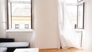 Una habitación con ventana, un radiador, una mesa con un objeto circular y un sofá gris.