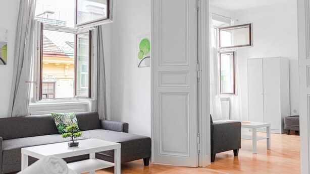 Una sala de estar moderna con un sofá, una mesa de centro y una silla. Hay una puerta que conduce a otra habitación.