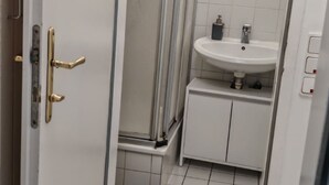 A bathroom with a white sink, a glass shower enclosure, and a door with a brass handle.