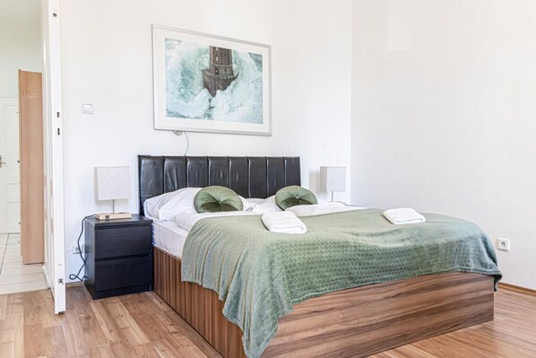 Een slaapkamer met een bed, nachtkastjes, een nachttafel, een lijst met een afbeelding en een deur.