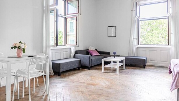 Ein modernes Wohnzimmer mit einer Couch, einem Esstisch mit Stühlen und großen Fenstern.