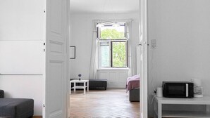 Ein Zimmer mit Bett, kleinem Tisch, Fenster mit Vorhängen, einer Mikrowelle und einer Kaffeemaschine.