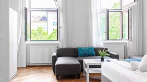 A modern living room with a grey sofa, a white coffee table, and a view of greenery outside.
