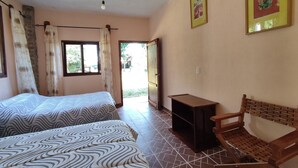 A room with two beds, a wooden chair, a small table, and a door leading outside.