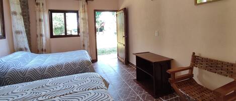 A room with two beds, a wooden chair, a small table, and a door leading outside.