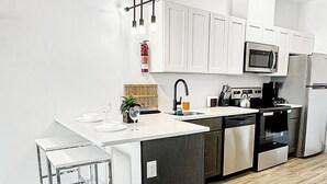 A modern kitchen with white cabinets, a central island with bar stools, a microwave, a refrigerator, and a sink. - Cozy King 1BR w/ Pool + Gym Near EWR & MetLife (Elizabeth)