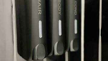 A row of black, rectangular dispensers labeled "HAIR," "BODY," and "COND" mounted on a tiled wall.