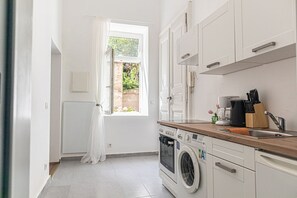Une cuisine équipée d’un lave-linge, d’une machine à café et d’une fenêtre donnant sur un espace verdoyant.