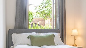 A neatly made bed with white bedding and a green pillow, a bedside lamp, and a window with curtains.
