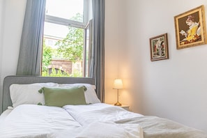 Une chambre à coucher avec un lit, une fenêtre, une lampe et deux tableaux encadrés accrochés au mur.