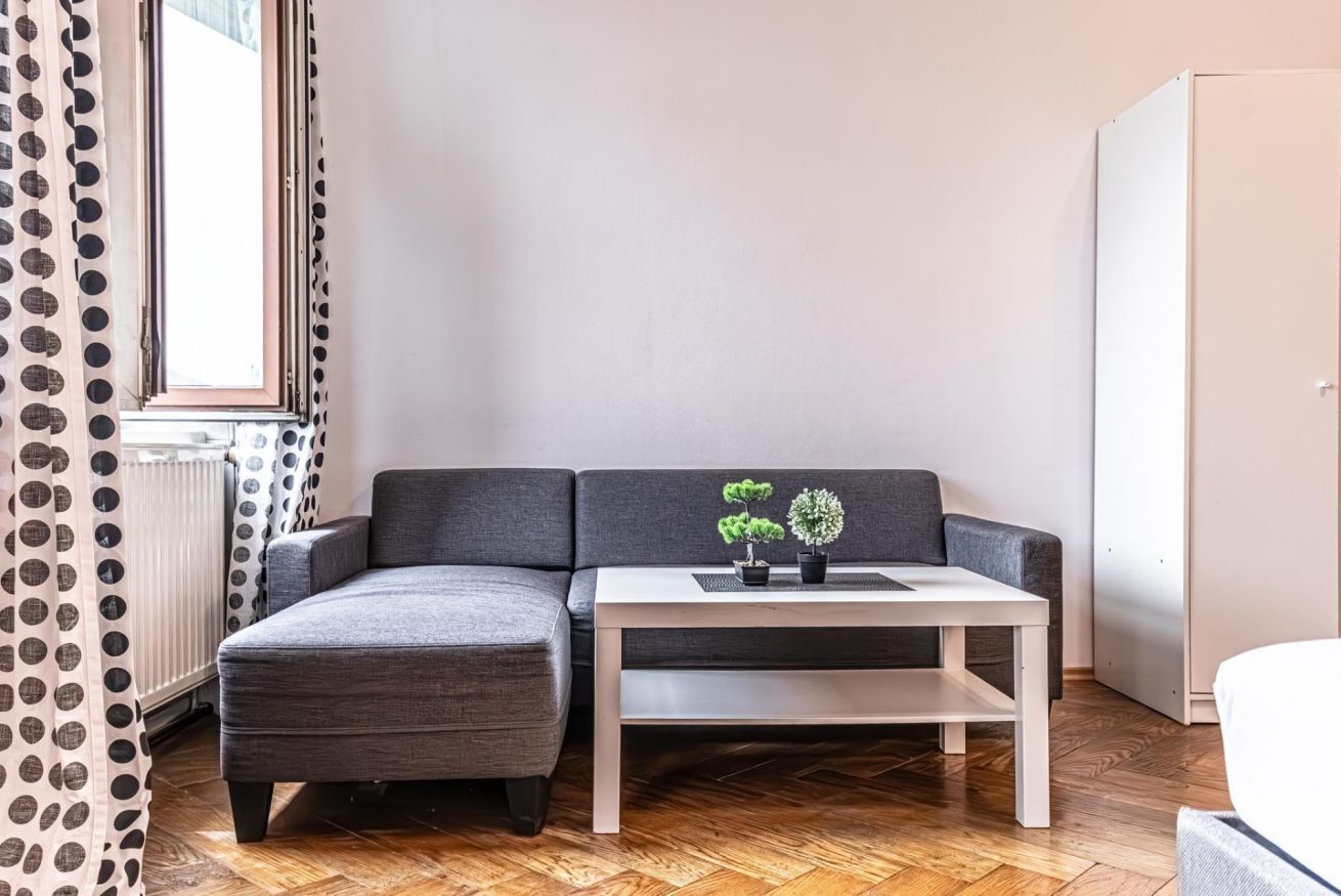 Een moderne woonkamer met een grijze bank, een witte salontafel en twee potplanten.