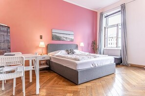 Une chambre à coucher avec un lit, un bureau, des chaises, une lampe et une fenêtre avec des rideaux.