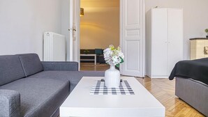 Een moderne woonkamer met een grijze bank, een witte salontafel met een bloemenvaas, een witte kledingkast en een houten vloer.