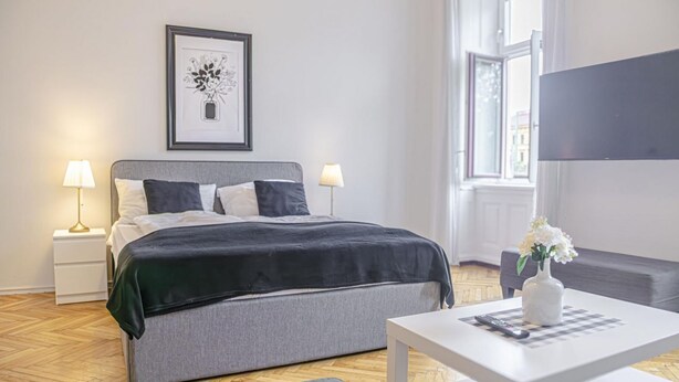 Een moderne slaapkamer met een bed, nachtkastjes, een bureau, een vaas met bloemen en een ingelijste foto aan de muur.