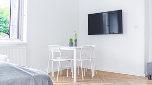A room with a bed, a table with chairs, a potted plant, and a mounted TV. - Classy 2BR Apt. w/ Exclusive Location near AKH (Wien)