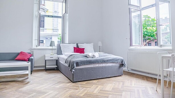 A bedroom with a bed, a bench, a nightstand, a lamp, and large windows. - Classy 2BR Apt. w/ Exclusive Location near AKH (Wien)