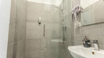 Une salle de bain avec une douche à parois de verre, un lavabo blanc et un sèche-cheveux fixé au mur.