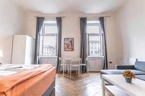 Una camera d'albergo con un letto, un tavolo, due sedie, un divano, una pianta in vaso e un quadro appeso al muro.