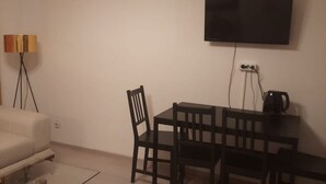 A room with a flat-screen TV mounted on the wall, a small table with chairs, a lamp, and a coffee maker. - Affordable 2BR Apt. Near Rennweg & Belvedere (Vienna)