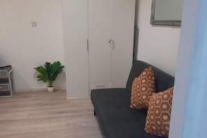 A room with a black sofa, patterned cushions, a potted plant, a wardrobe, and a small table. - Modern Apart. - Huge Longstay discount (Wien)