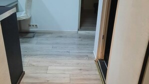 Een gang met houten vloer, een witte muur en een deur naar een andere kamer.