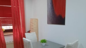 Een eetruimte met een tafel, stoelen, een potplant, een rood gordijn en een schilderij aan de muur.