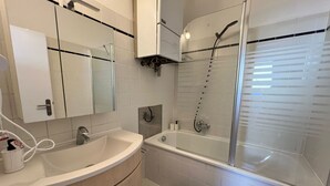 Ein Badezimmer mit weißem Waschbecken, einem Spiegel, einer Duschkabine aus Glas und einer Badewanne.