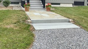 Een modern huis met twee verdiepingen, een veranda, een donkerbruine voordeur en een pad van stenen dat naar de ingang leidt.