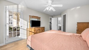 Una camera da letto con un letto, una ventola a soffitto, una TV e un comò in legno.