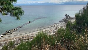 A coastal landscape with a rocky shoreline, clear water, and distant mountains. - Huckleberry Hideaway - an idyllic off-grid cabin on Savary Island, BC. Canada. (Lund)