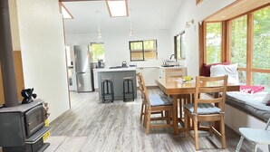 A cozy kitchen with a central island, wooden dining table, and bar stools. - Huckleberry Hideaway - an idyllic off-grid cabin on Savary Island, BC. Canada. (Lund)
