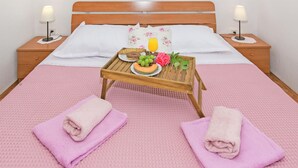 Una cama bien hecha con un edredón rosa texturizado, una mesita de noche de madera con una bandeja de desayuno y dos lámparas de noche.