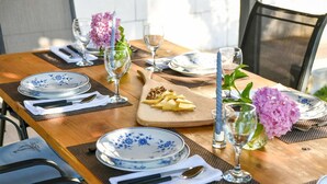 Una mesa de comedor de madera adornada con platos florales azules, cubiertos y vasos, junto con una bandeja de frutas y flores.